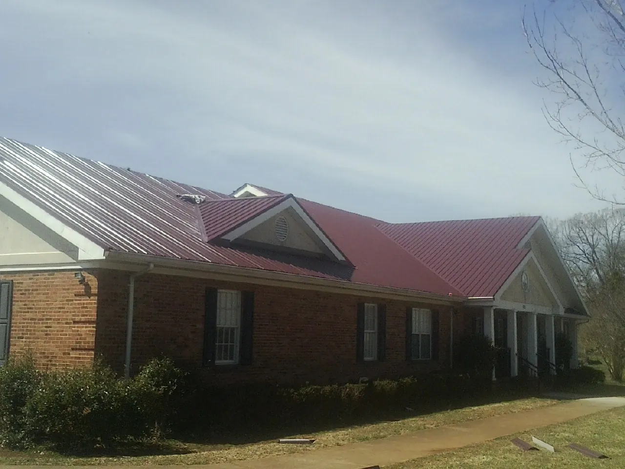 Red metal roof with gabled entries on a long brick building, from a Hail Damage Roof Repair job in Clatskanie