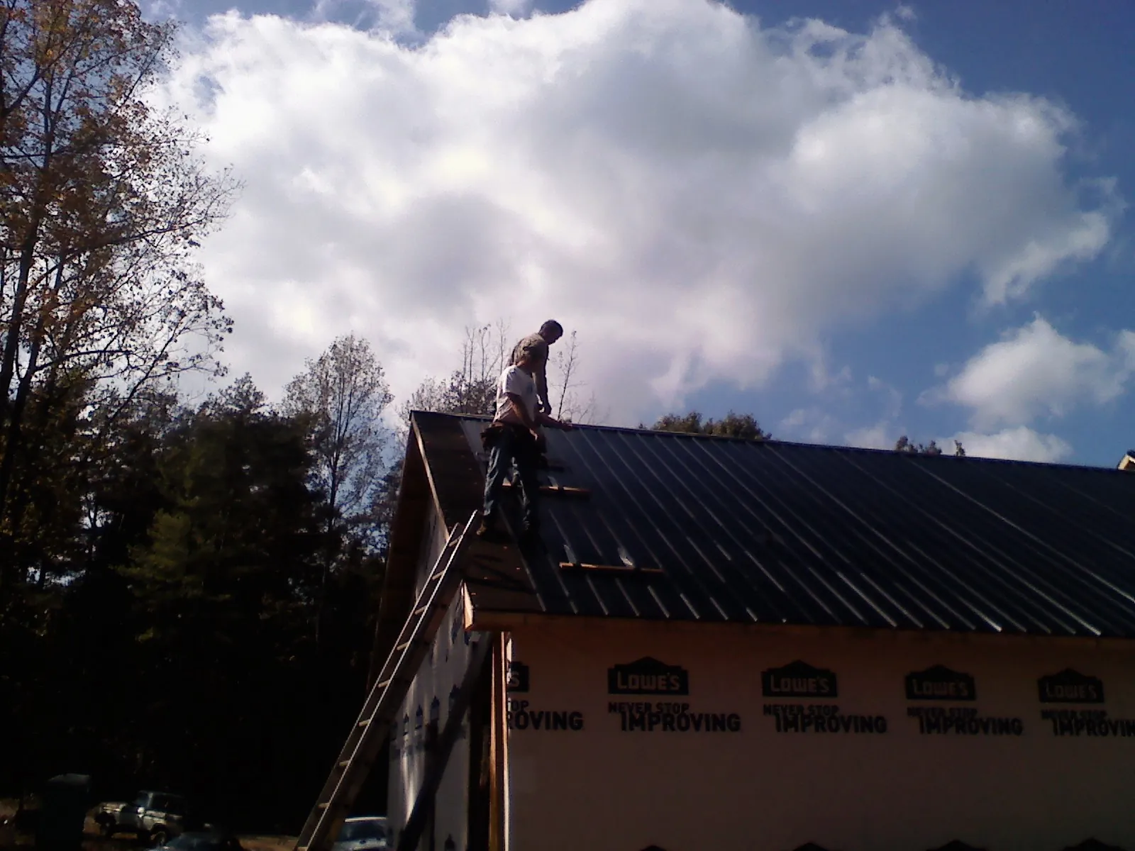 Roofer fastening dark metal panels high against a cloudy sky, from a Roof Inspection job in Clatskanie