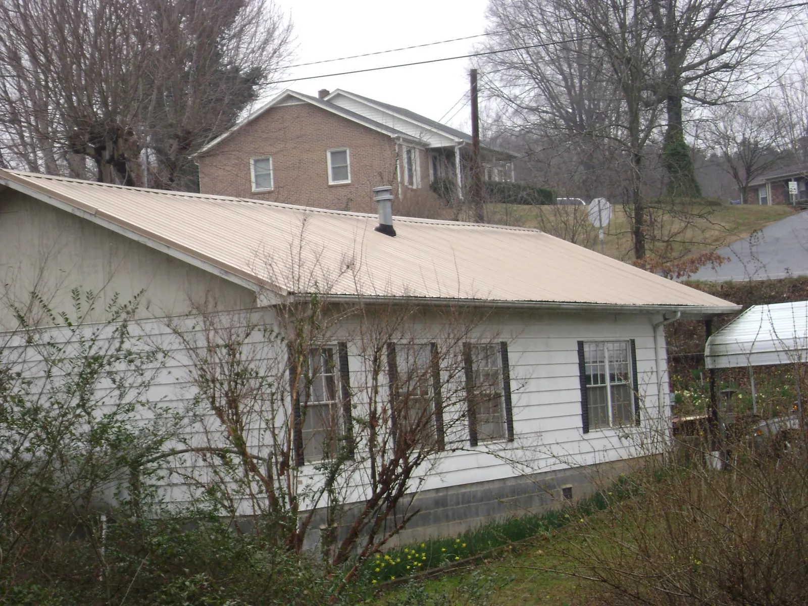 Tan metal roof on a white sided house set into a hillside — Commercial Roofing by Roofing Brothers in Clatskanie